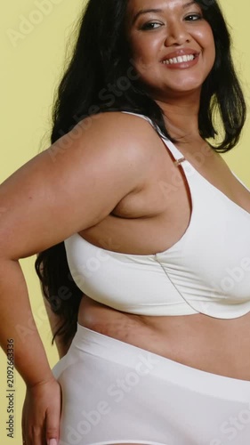 Vertical video: Posing model smoothing underwear while camera panning in studio, showing white bra