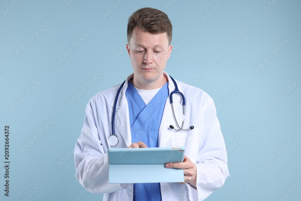 Fototapeta premium Doctor with stethoscope using tablet on light blue background