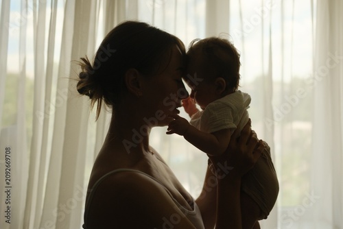 Foto ilhouette of a mother lifting her baby up in front of a window, cozy home atmosp