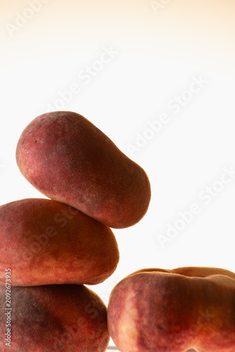 Dark smooth peaches stacked in a tower against a warm glowing background. Minimal zen still life composition, earthy tones, balance and calm concept.