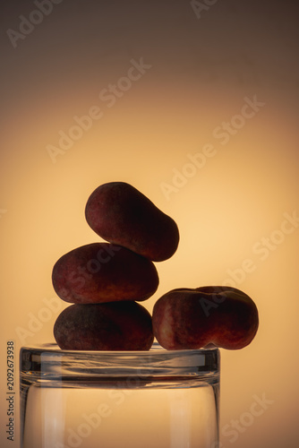 Dark smooth peaches stones stacked inside and around a glass jar in warm amber studio light. Zen minimal still life, earthy tones, spa and wellness concept.