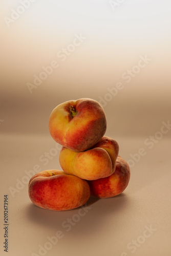 Flat peaches and a halved peach scattered on a warm neutral background. Natural loose arrangement, studio still life showing fruit texture and interior.