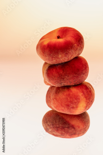 Four flat peaches stacked in a tall vertical tower on a neutral warm background with copy space. Classic minimal fruit composition, studio still life.