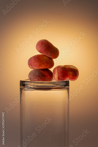 Flat peaches stacked above and inside a glass jar in warm golden studio light. Creative fruit and glassware composition, autumn warm tones, copy space.