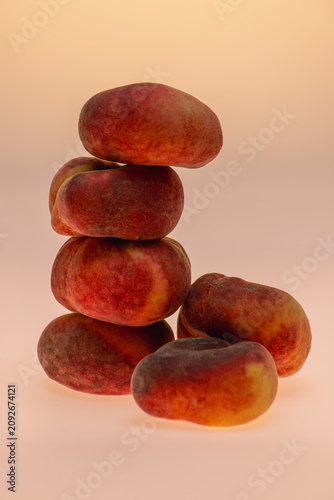 Creative still life of four flat peaches stacked in a tower on a warm peach-toned background. Playful fruit composition, studio photography with copy space.