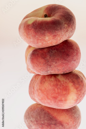 Stack of flat peaches on white background with soft reflection below. Clean minimal studio still life, reflective surface, summer fruit composition.