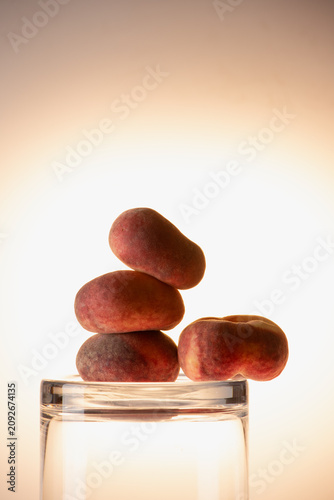 Flat peaches and smooth stones arranged around a glass jar in warm soft studio light. Mixed object still life, earthy organic composition with copy space.