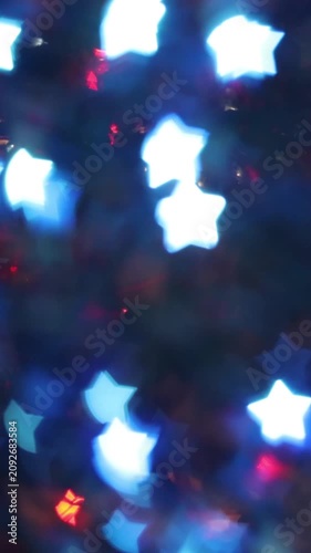 Glowing white blue star-shaped bokeh lights on dark magical night background creating festive winter holiday celebration atmosphere abstract decoration texture for greeting card design.