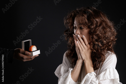 Obraz na płótnie Surprised young female with curly hair receiving unusual sushi ring gift