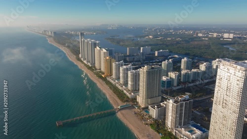 Aerial drone footage captures Sunny Isles Beach Miami at golden hour with luxury high-rise condominiums lining Atlantic Ocean coastline.
