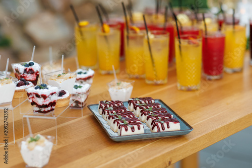 Catering buffet table with sweet mini desserts in cups and refreshing cocktails.
