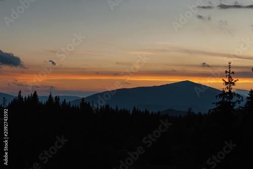 Beautiful evening twilight with bright orange sky above dark mountain ridges.