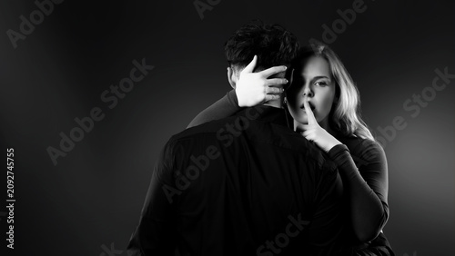 Foto Woman holding finger to lips gesturing silence while embracing a man from behind