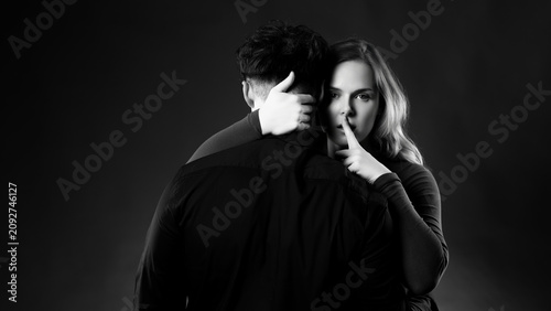 Schilderij op canvas Woman shushing, keeping a secret while embracing a man in a black and white stud