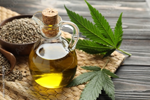 Cuadro en lienzo Hemp oil, seeds and leaves on black wooden table, closeup