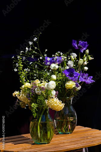 Colourful beautiful flowers in bloom inside glass vases on wooden table interior