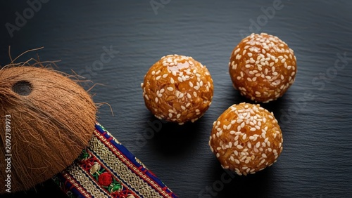 Gourmet coconut drops with caramel sheen and sesame seeds on black slate against deep negative space