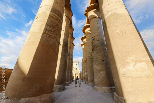 Tourists and Egyptian guides walk through the Grand Colonnade Hall of papyrus bud columns at the Great Court of Ramses II, at Luxor Temple, Luxor Egypt.