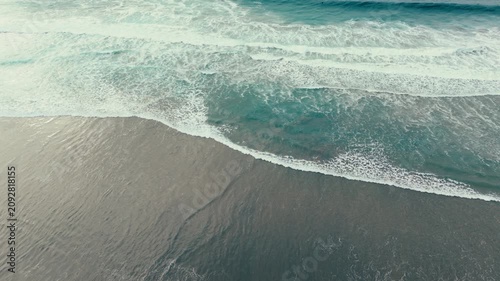 Aerial drone view of ocean waves rolling onto Pacific Beach shoreline in San Diego California under cloudy skies
