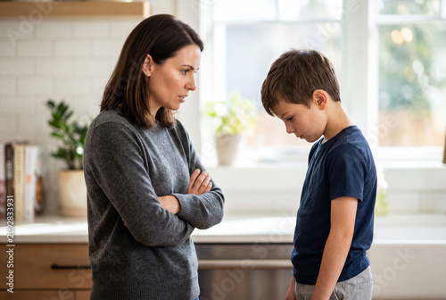 Serious mother disciplining her young son standing in modern kitchen at home
