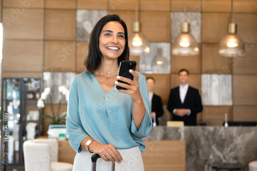 Foto Hotel guest standing in lobby with suitcase, using mobile application on smartphone to check reservation details and booking confirmation before check-in