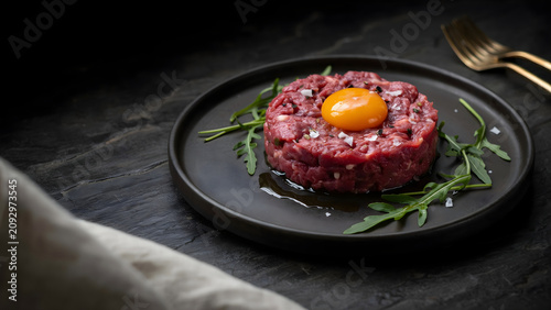 Gourmet beef tartare with raw egg yolk and fresh arugula on a dark plate