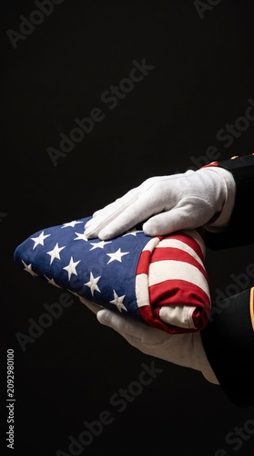 Honor guard hands in white gloves holding folded American flag against black background during military funeral ceremony