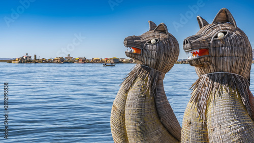 The traditional balsa de totora has decorations in the shape of puma heads woven from reeds on the bow of the boat. On the far shore, you can see the Uros floating island, village buildings. Blue lake