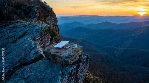 Remote work concept featuring modern laptop and smartphone on rugged mountain cliff edge during spectacular sunset landscape.