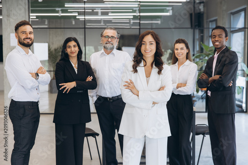 Diverse business team smiling with arms crossed, standing together in modern office, showing teamwork and unity