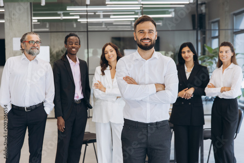 Diverse business team standing in office with male leader crossing arms, symbolizing successful corporate teamwork and professionalism