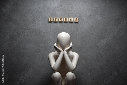 Faceless figure sitting under stress text on dark background symbolizing anxiety, burnout and emotional distress