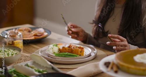 African American woman reaching for fork and knife, cutting roasted squash and eating at table