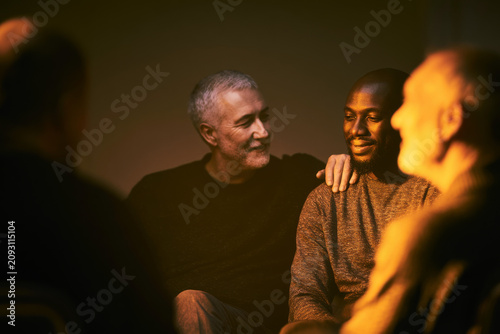 Authentic documentary scene of a men's mental-health support group in a community hall, one man comforting another with a hand on the shoulder, warm and unguarded, soft natural light, real connection 