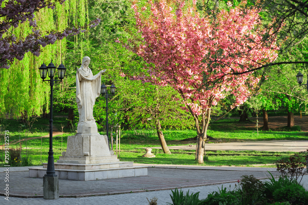 Obraz premium Serene religious sculpture stands amidst vibrant spring blossoms in a park