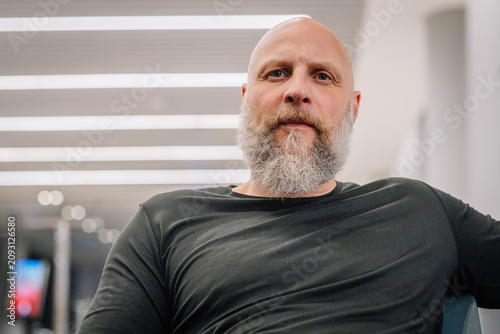 Konstfotografi Bald Caucasian man with a full beard wearing a black shirt sits in a modern indo