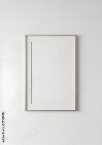 Empty white picture frame with silver frame against a plain white wall. Empty picture frame hanging on a white wall.
