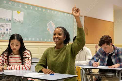 Fotografie Happy student raising hand to answer question during a lesson in a modern high s