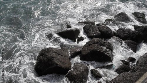 Obraz na plátne Ocean waves crashing against dark coastal rocks with white foam