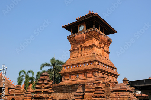 The iconic Menara Kudus mosque tower made of red bricks under a clear blue sky, a historic heritage site blending hindu and islamic architecture in Kudus, Central Java, Indonesia.