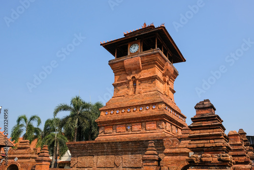 The iconic Menara Kudus mosque tower made of red bricks under a clear blue sky, a historic heritage site blending hindu and islamic architecture in Kudus, Central Java, Indonesia.