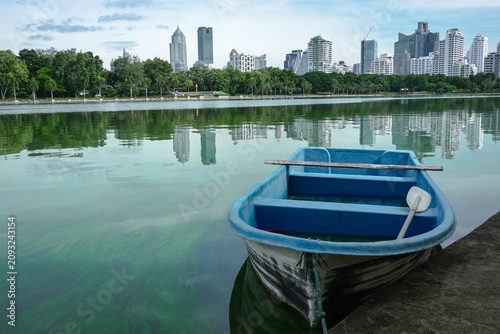 Fotografía A blue boat in river and the silhouettes of high-rise buildings reflect Bangkok