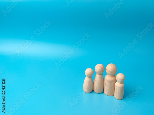 Four simple, blank wooden peg dolls of varying heights stand grouped together in a line against a blue background