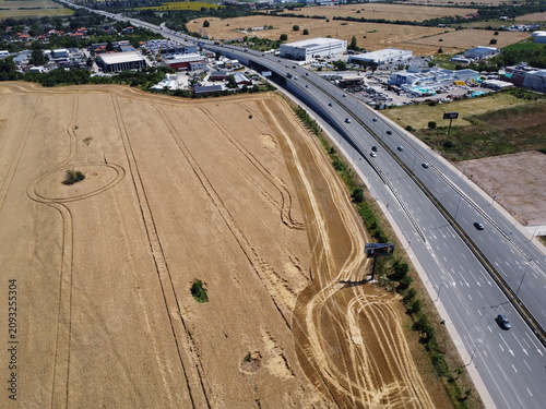 Photography Drone shot of country road dividing harvested field with a lonely tree and agric