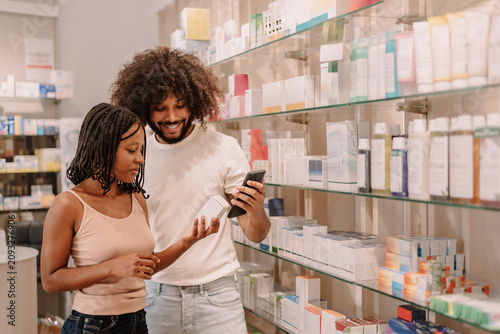 Young African American couple choosing medicine with smartphone in pharmacy