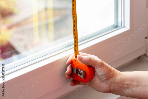 Person measuring white window frame with a yellow tape measure