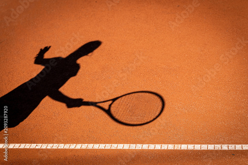 Schatten eines Tennisspielers mit Tennisschläger auf einem Sandplatz als kreatives Symbol für Tennissport, Bewegung und Wettkampf.