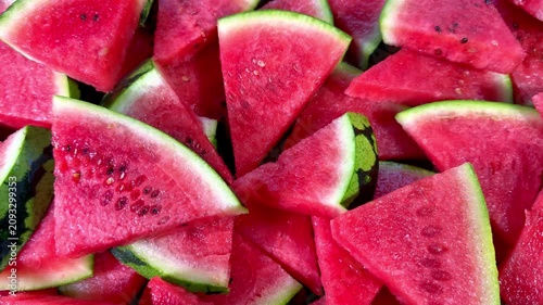 Closeup pan shot of water melon or watermelon, which has been cut into triangular slices, with thick green outer skin and juicy pink fruit, ready to eat.