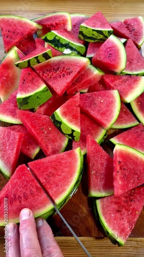 Vertical video social media - Closeup of a man’s hands using a knife to cut a juicy water melon or watermelon into triangular slices of pink fruit, ready to eat.