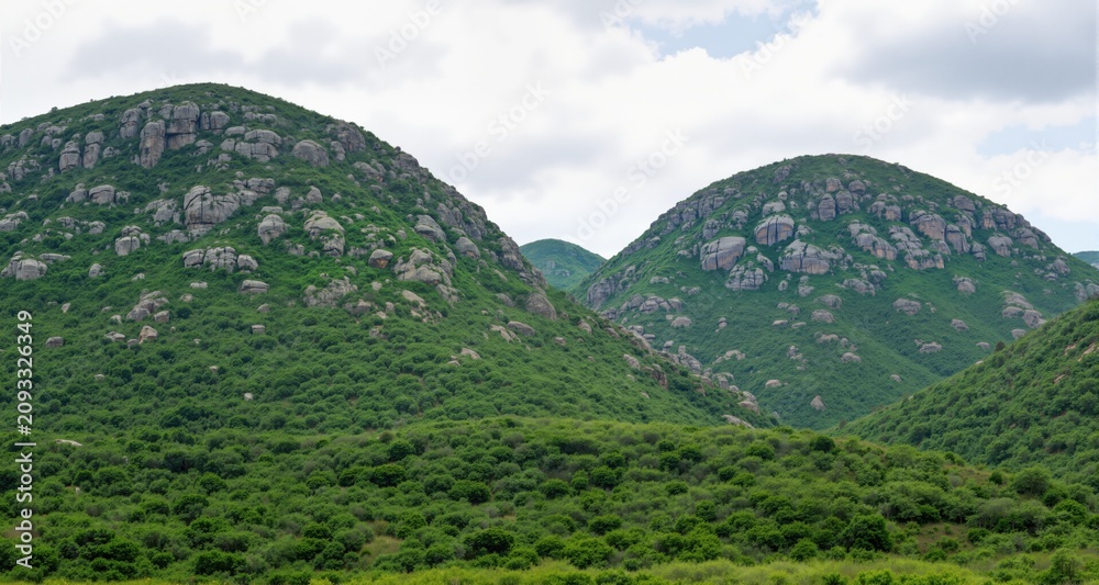 Obraz premium Beautiful landacape view of large green rocky hills against light cloudy sky 